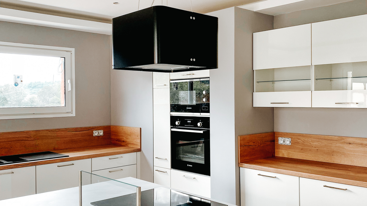 cuisine avec un grand plan de travail intégrant plaque de cuisson et hotte décorative suspendue